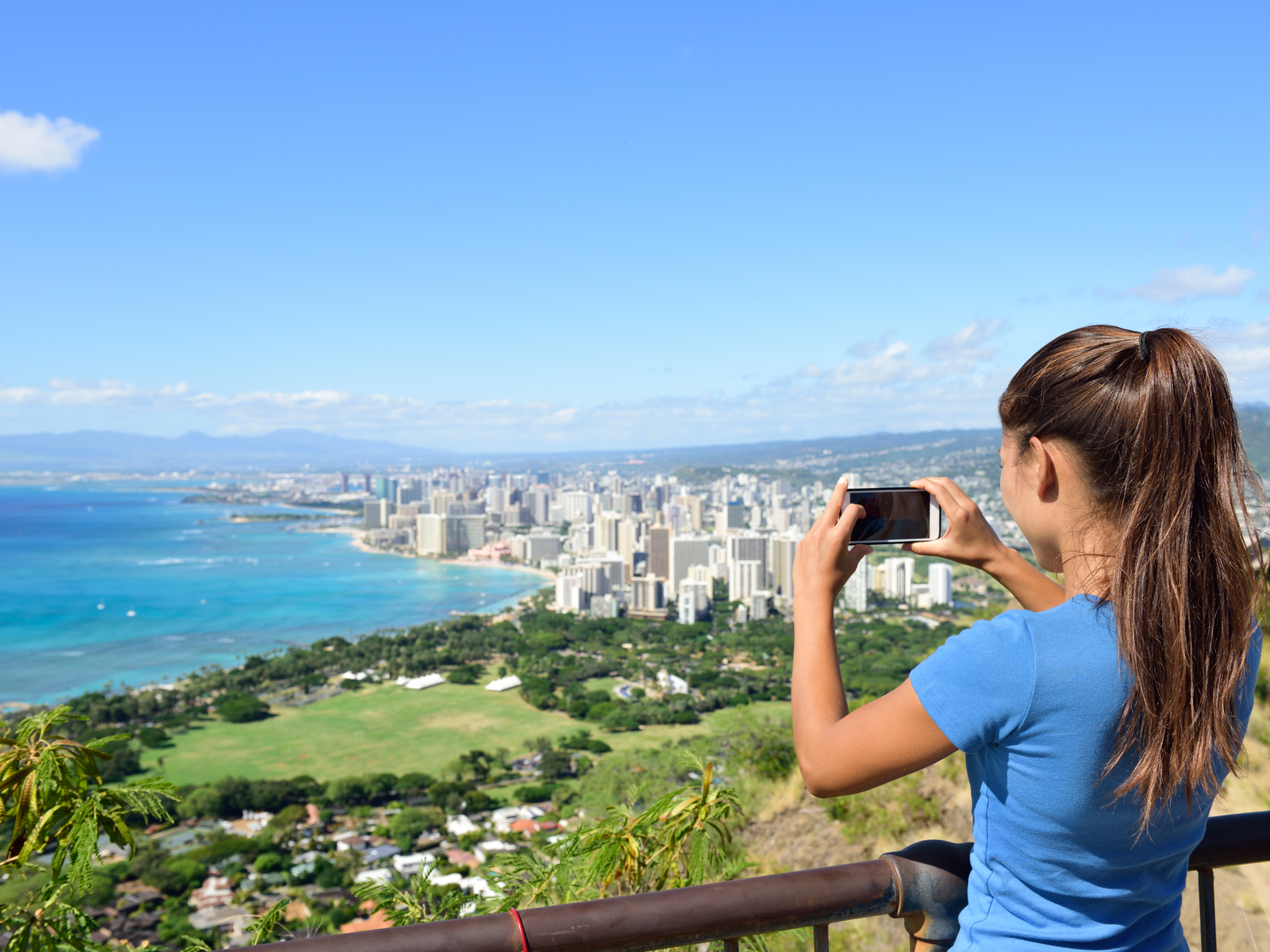 A skinny woman taking a picture of Waikiki Beach and downtown Honolulu from the overlooking Diamond Head, one of the best things to do in Oahu
