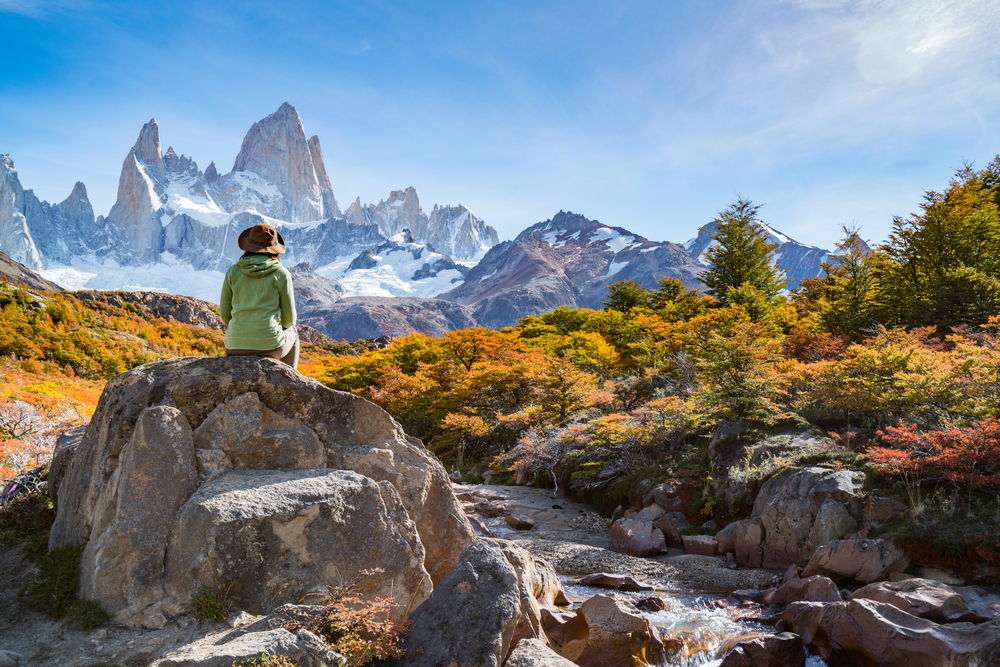 Woman hiking in Patagonia during the best time to visit and sitting on a rock overlooking a stream
