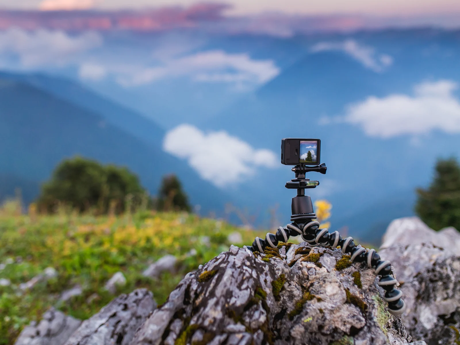 Action cam sitting on a rock with a bendy stand holding it up and a mountain in the background