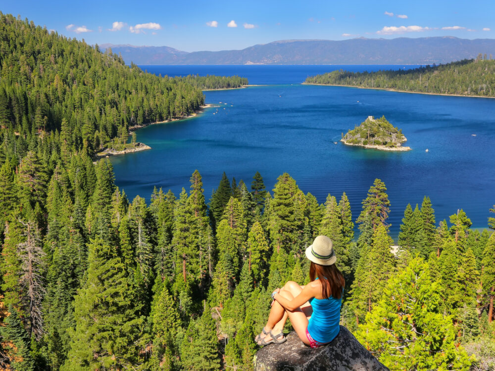 Woman sitting holding her legs while sitting on a rock enjoying a view of Emerald Bay for a piece titled Where to Stay in Lake Tahoe