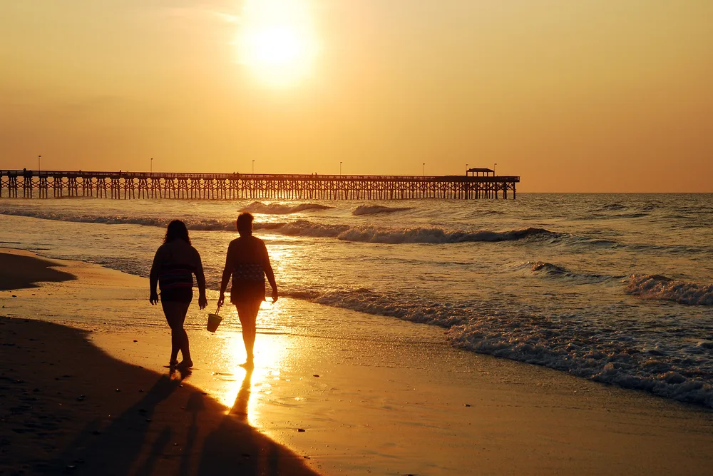 People taking a sunrise stroll along a beach while the sun sets