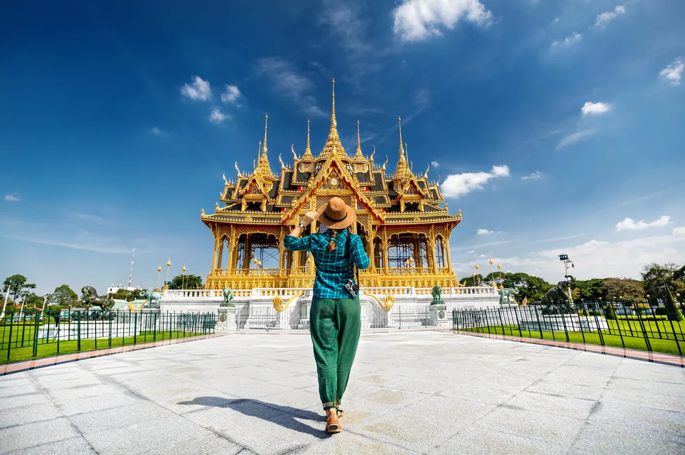Woman in Thailand traveling alone holding a hat in front of a temple