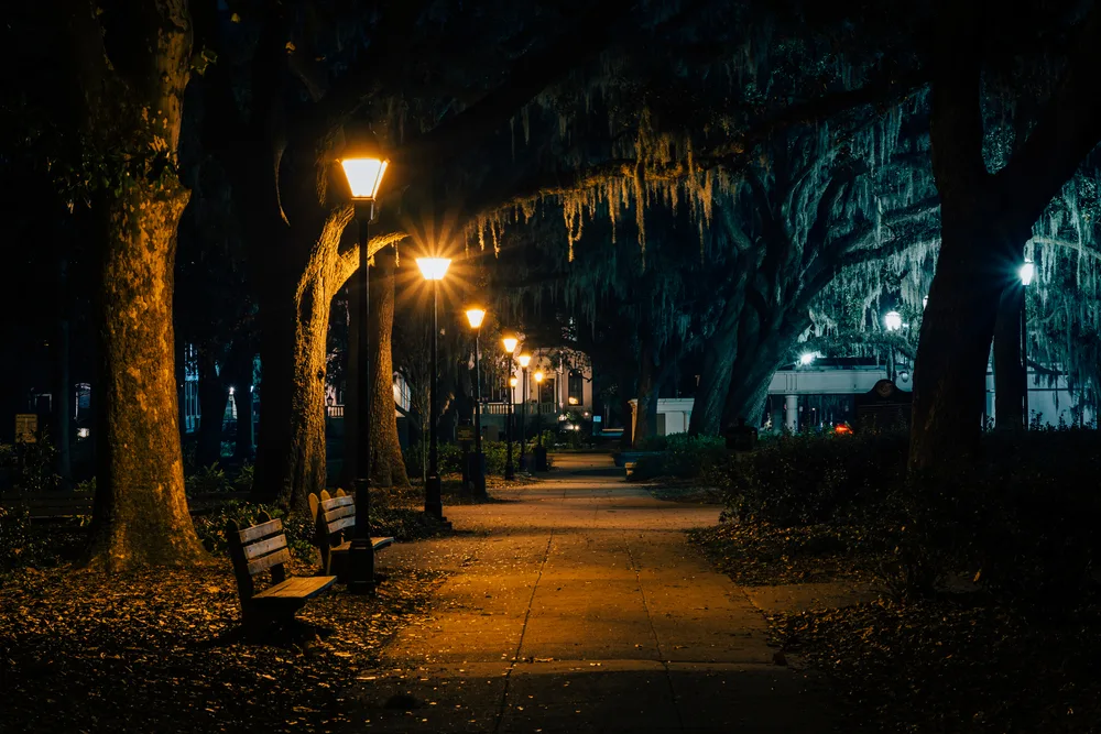 Benches and trees with Spanish moss along a walkway at night, at Forsyth Park, in Savannah, Georgia