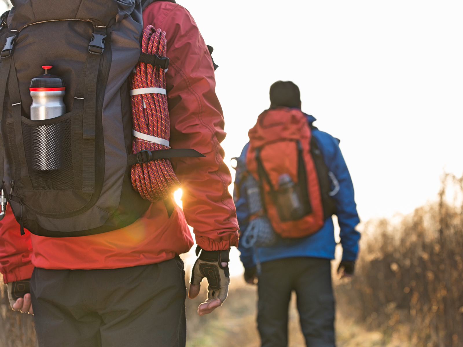 Two folks wearing the best hiking backpacks with ropes and blue and red jackets with the sun in the distance