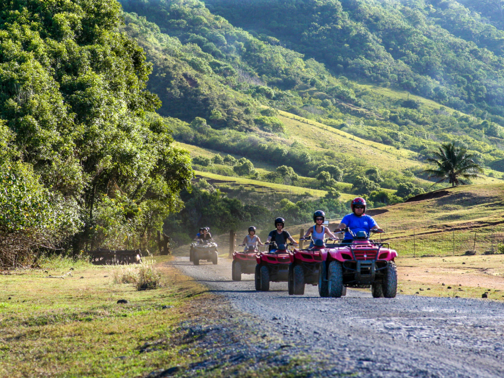 A group of friends riding ATVs on the bare road at Kualoa Ranch, one of the best things to do in Oahu, with the sloppy natural trail in the background