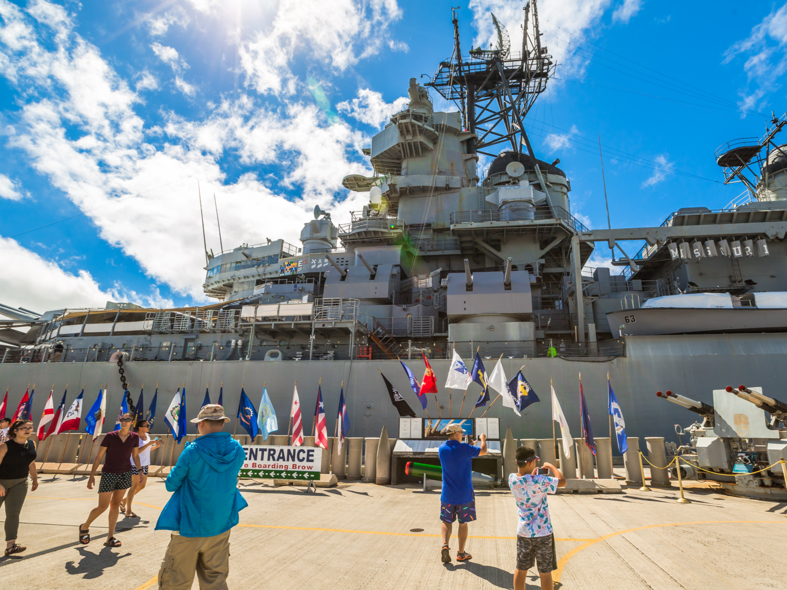Several tourists taking pictures of the historic USS Missouri BB-63 warship at Pearl Harbor National Memorial, one of the best things to do in Oahu, with many flags lined up at the front