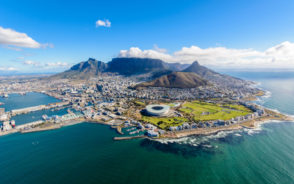 Featured image for a piece on Is Cape Town Safe to Visit featuring an aerial shot of the city with its round stadium and coastline next to the mountain