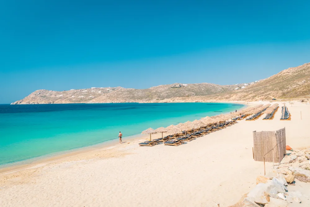 Elia Beach, one of our top picks for where to stay in Mykonos, pictured with chairs on the beach with a guy walking next to the water