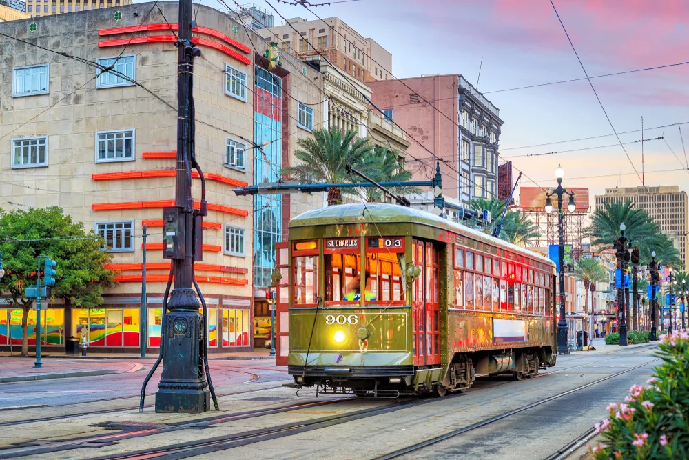 A streetcar traversing its rails in the middle of the city during a sunset, taking a short ride on it is one of the best things to do in New Orleans in our list.