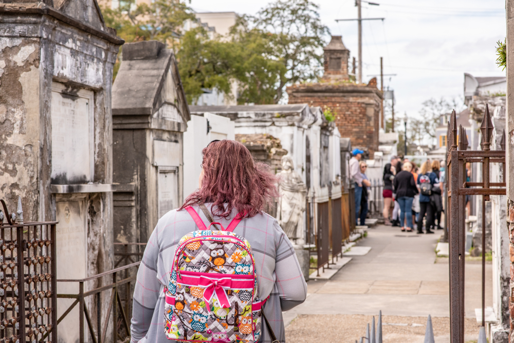 A woman walking in on a cemetery in broad daylight and others are gathered in one place inside for a cemetery tour, one of the best things to do in New Orleans.