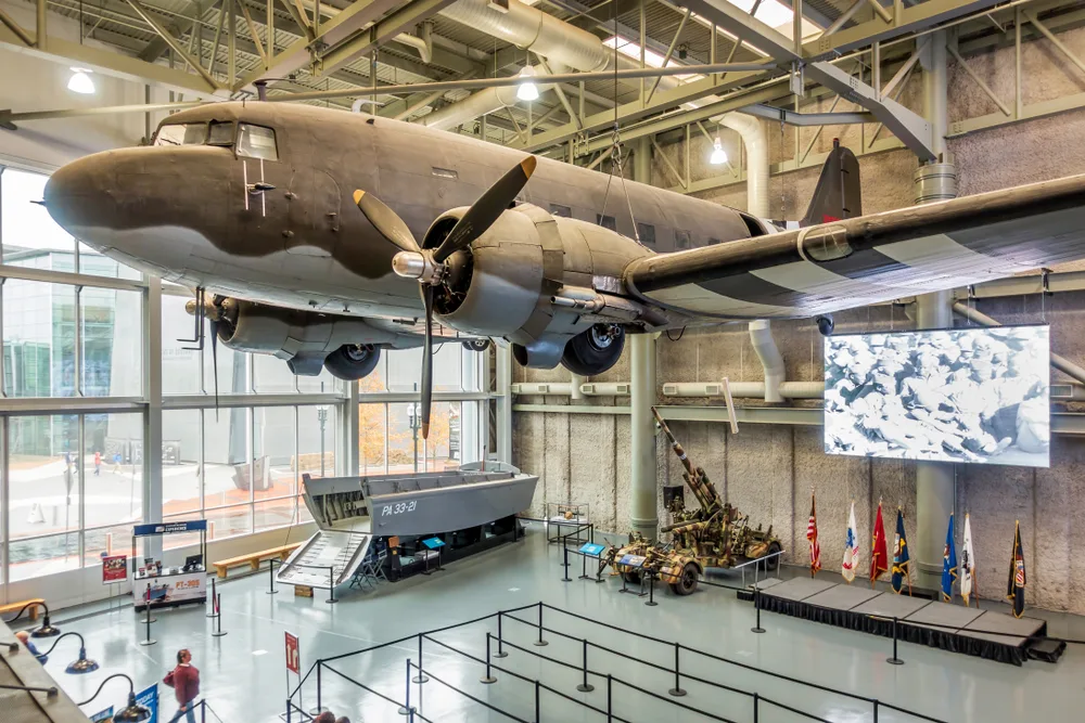 A large old war airplane hanging by the ceiling and other war artifacts are on the ground in the National WWII Museum, one of the historic things to do in New Orleans.
