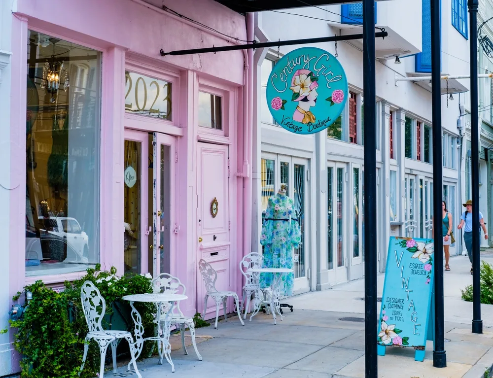 A side of the Magazine Street where one store has pink storefront with feminine floral signage and old metal chairs and tables, one of our picks on the things to do in New Orleans.