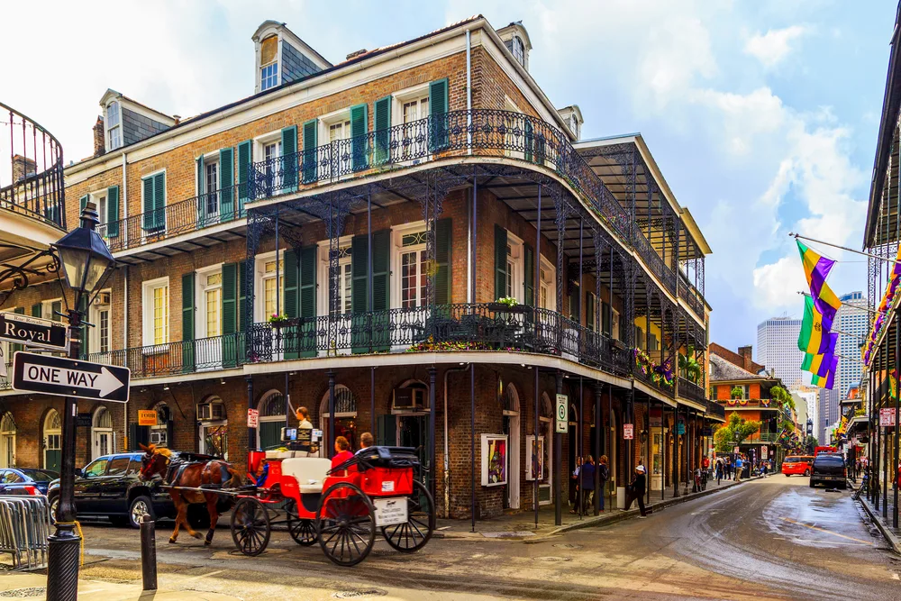 The old French Quarter building located in a street corner where a horse carriage is passing by with passengers, one of the historic destinations in our list of things to do in New Orleans.