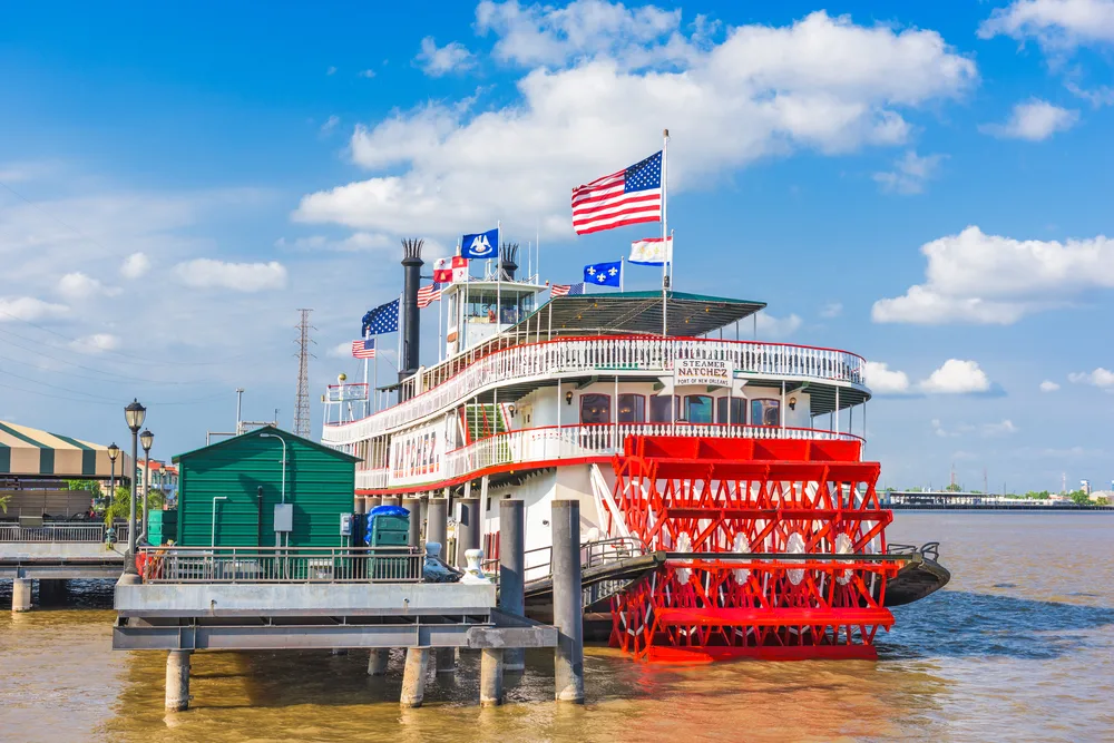 The Steamboat Natchez with various flags including one for the US, docked on a port, having a tour with it is one of the best things to do in New Orleans.