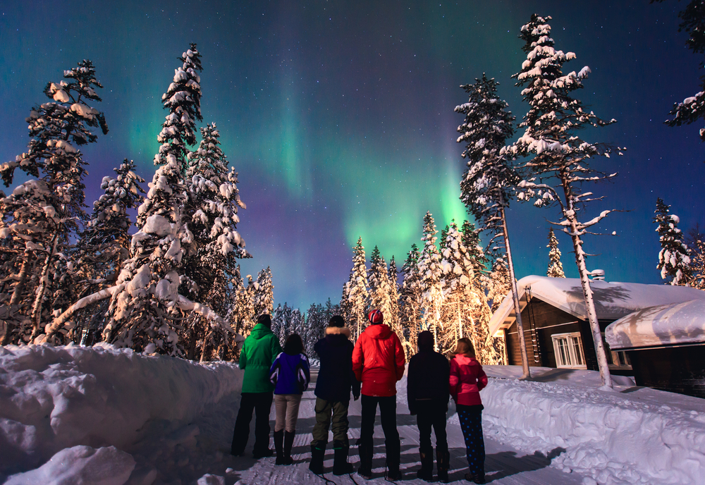 Family standing outside looking up at the Northern Lights from one of the best places to visit in Alaska