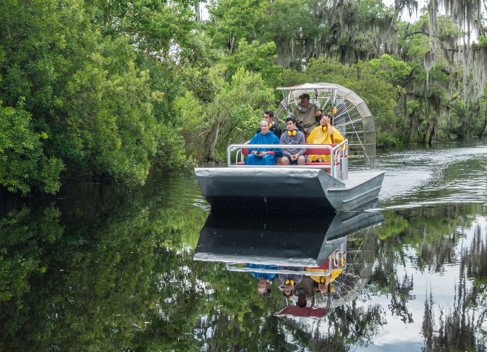 A small boat traversing a swamp with trees on the side on a swamp tour, one of the best time to do in the New Orleans.
