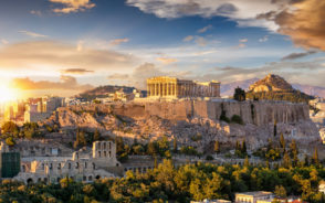 Image of the Acropolis of Athens on a hill with the sun rising over the cliffs for a piece on where to stay in Athens
