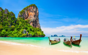 Featured image for a piece on where to stay in Phuket, Thailand with a few boats on the water by the cliffs