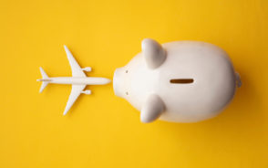 White piggy bank and airplane model depicting savings on flights covered in Scott's Cheap Flight reviews