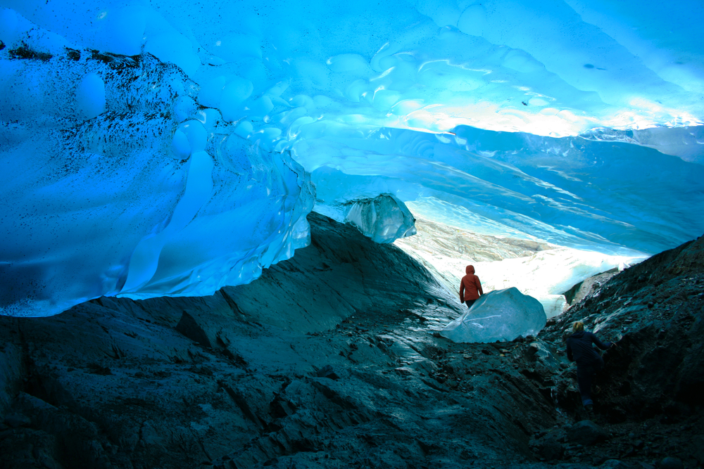 Explorer in an orange jacket inside Mendenhall Glacier, one of the best places to visit in Alaska, with black rocks and gorgeous views