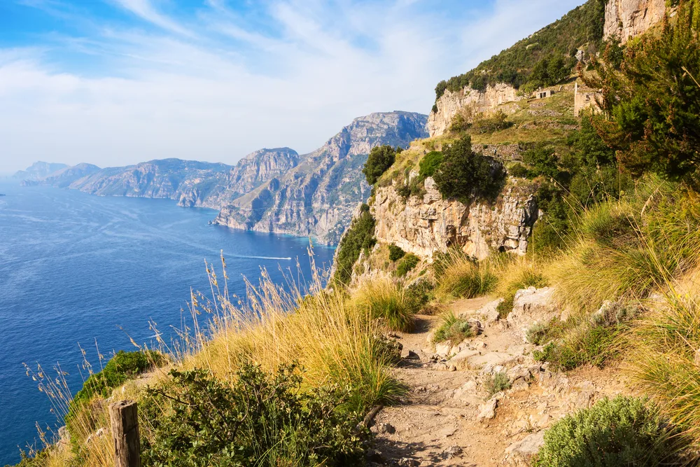 Gorgeous cliffside of Agerola, a top pick when thinking about where to stay in the Amalfi Coast, pictured overlooking the deep blue ocean with lines of clouds high in the sky during the summer