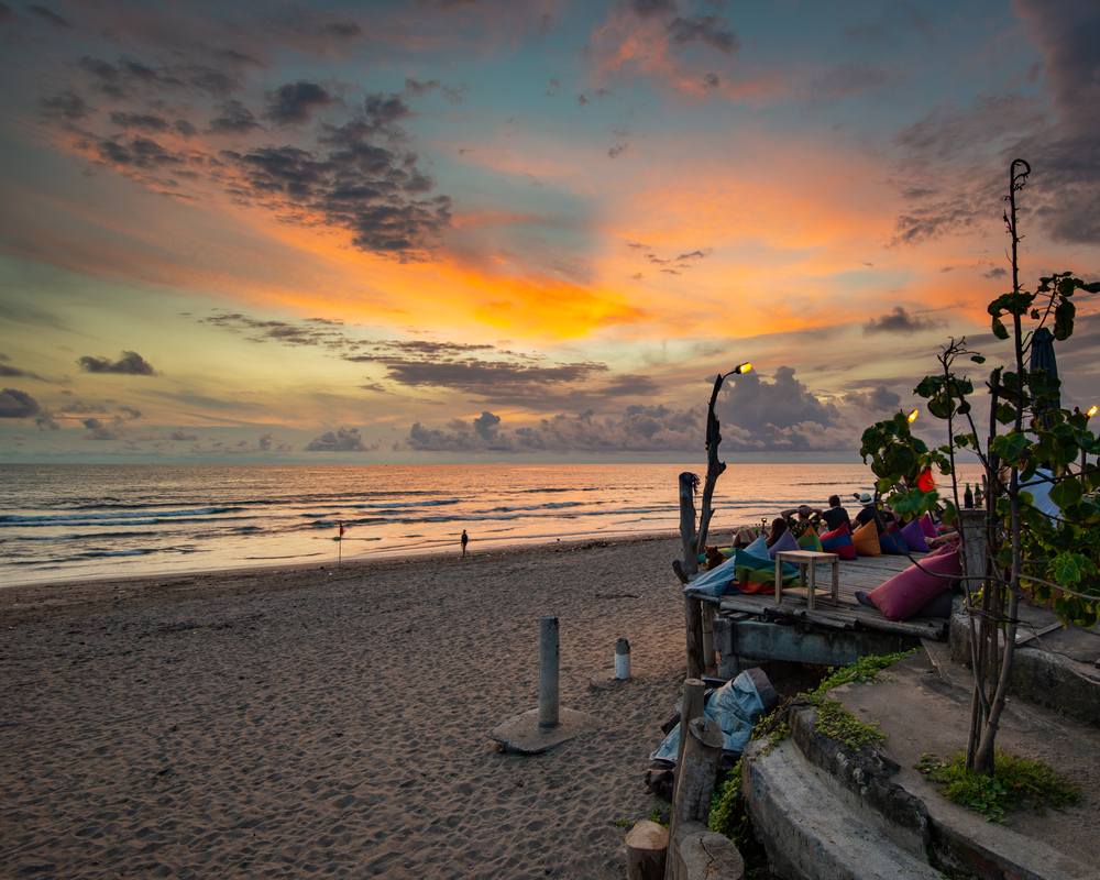 Gorgeous sunset photo of people lounging by the ocean at Seminyak, one of our top picks for where to stay in Bali