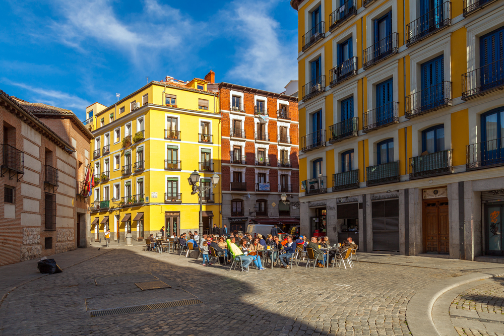 Image of La Latina, one of the best places to stay when visiting Madrid, as seen from the eyes of someone walking between the gorgeous yellow and orange buildings