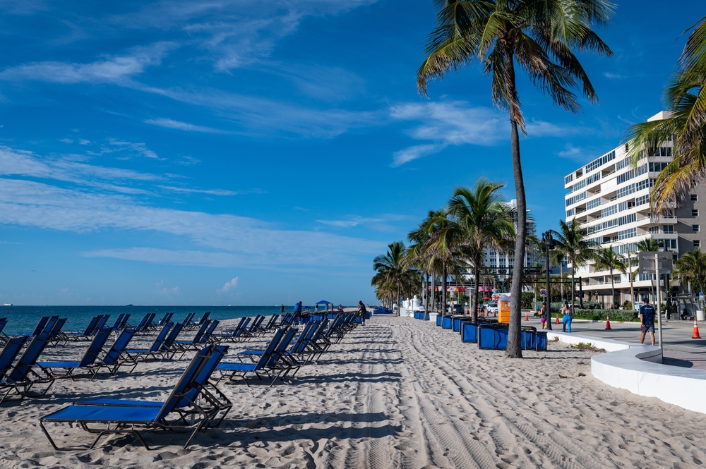 Central Beach, one of the best places to stay in Fort Lauderdale, pictured from the sandy beach with blue chairs on either side on a clear day