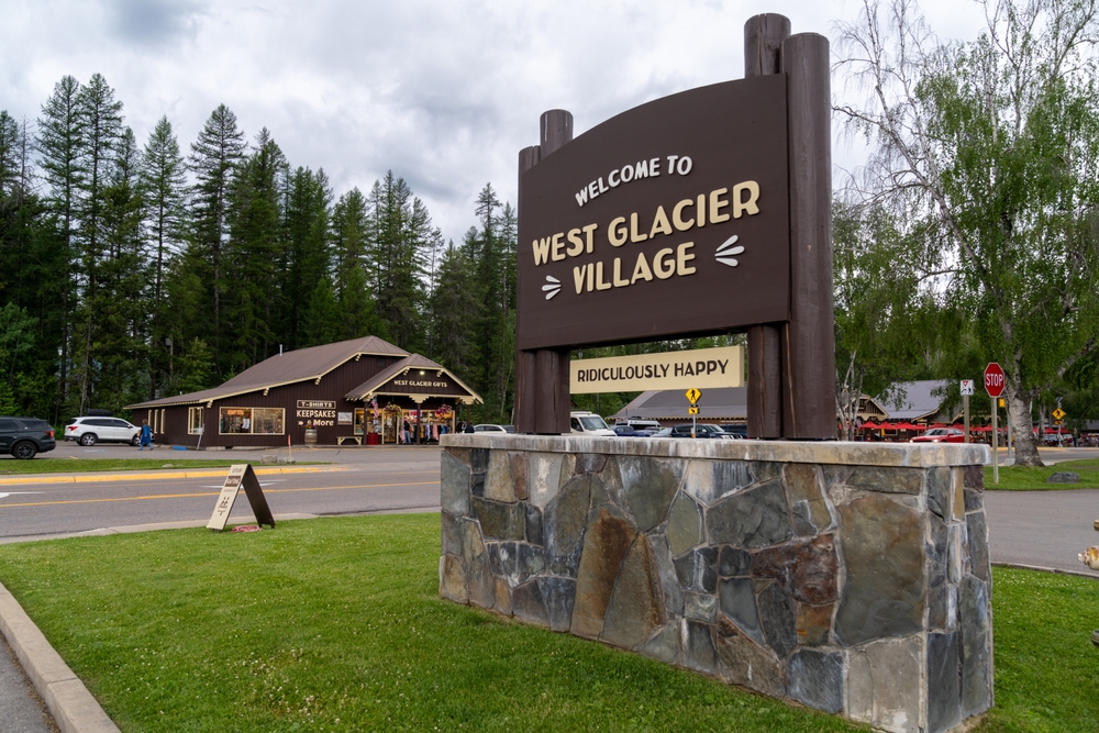 Sign that says welcome to West Glacier Village with a few small buildings around for a piece on where to stay when visiting Glacier National Park