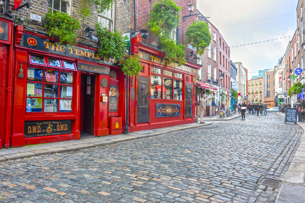 Several people walking around a red pub in Dublin during the best overall time to visit with a semi-cloudy sky