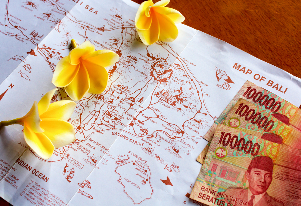 View of a map of Bali with several of the best places to stay on the island with flowers on it next to currency