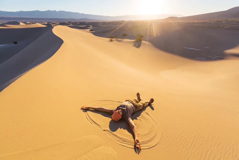 Guy doing a snow angel on the sand dune for a piece titled Where to Stay in Death Valley