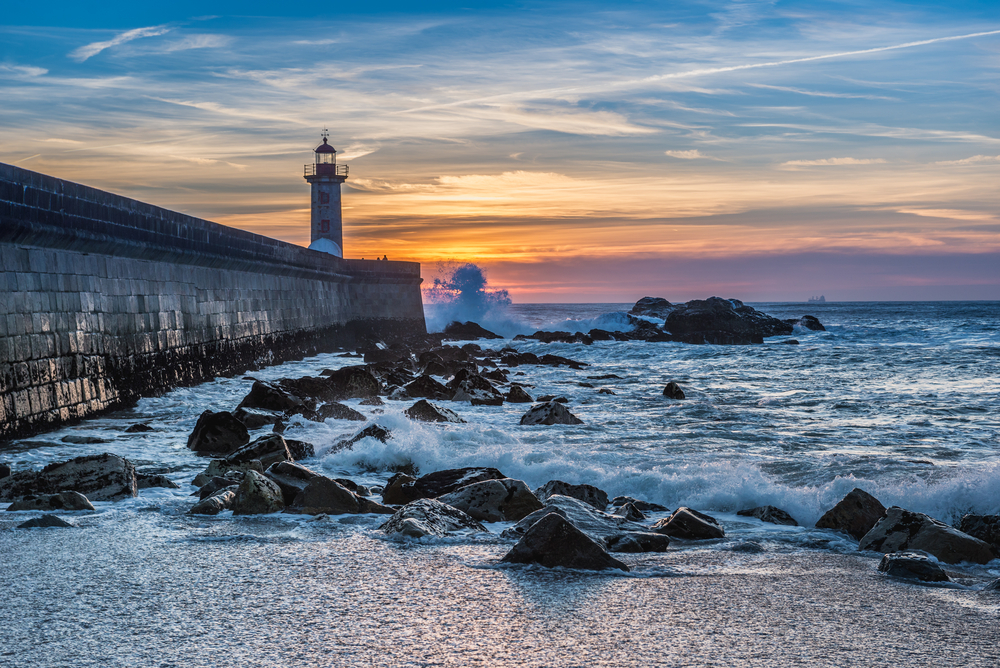 Foz do Douro pictured at dusk with waves crashing on the rocks next to a stone jetty for a piece on where to stay in Porto Portugal