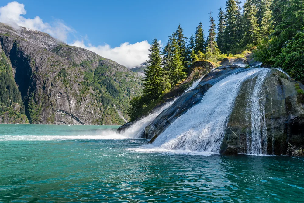 Tracy Arm Fjord, one of the best places to visit in Alaska, pictured from the view of a boat driver next to a gorgeous waterfall in the middle of a river