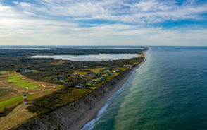 Gorgeous aerial shot of Nantucket pictured during the best time to visit with a sandy berm running along the lighthouse and by some nice homes