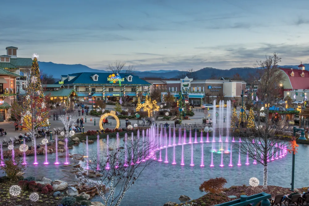 Neat aerial view of the downtown area in Pigeon Forge pictured during the best time to visit with a fountain with purple water shooting up and a cloudy sky in the background