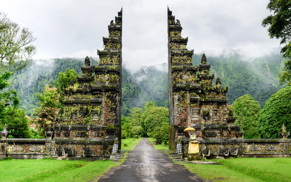 Gorgeous view of misty hills just beyond a temple-style gate behind which you can see mountains, pictured during the best time to visit Indonesia