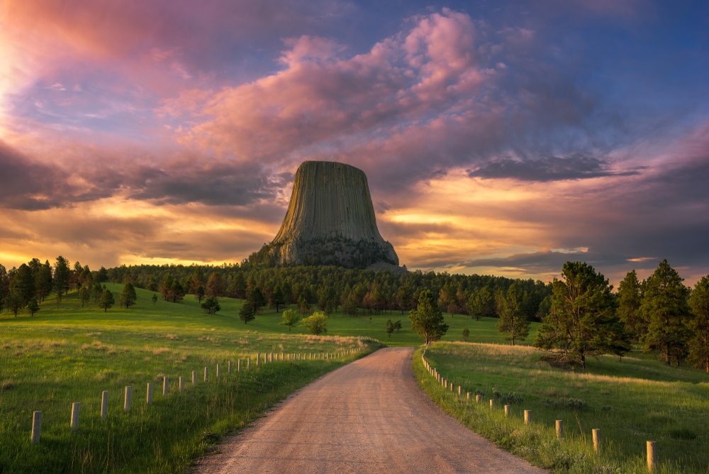 Sunrise at Devils Tower pictured from the point of view of someone walking on a dirt road during the summer, the best overall time to go to Wyoming