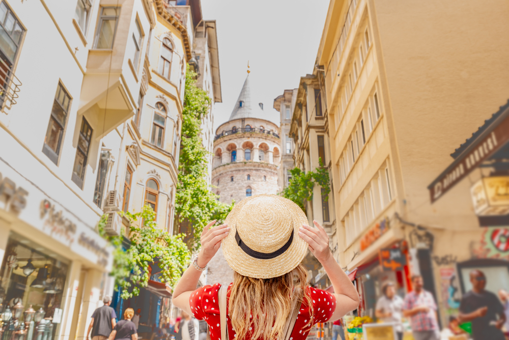 Woman holding her hat as seen from behind and looking at the Galata Tower in Beyoglu during the best time to visit Istanbul 