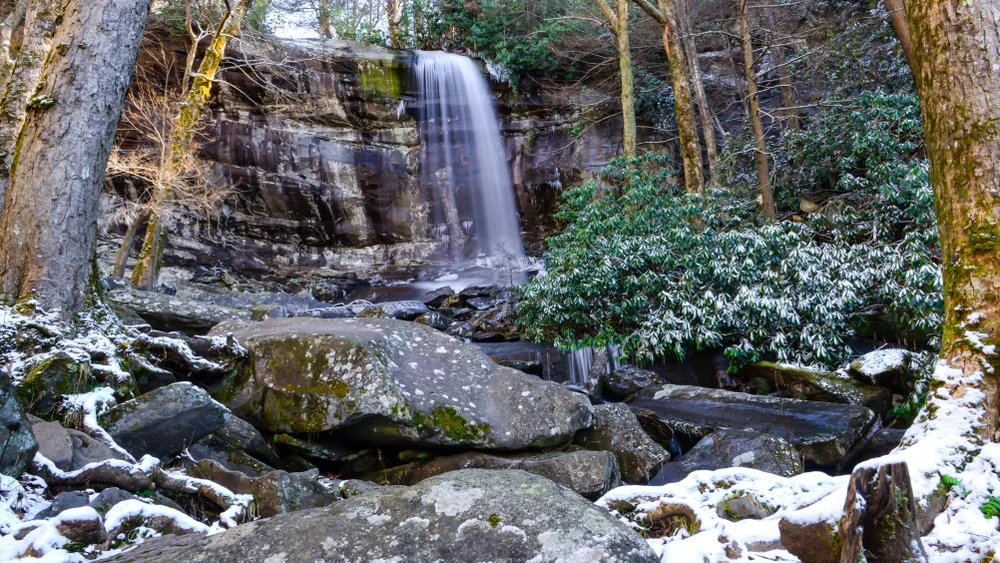Snow covering the ground by a waterfall in the forest of the smoky mountains during the cheapest time to visit Pigeon Forge Tennessee