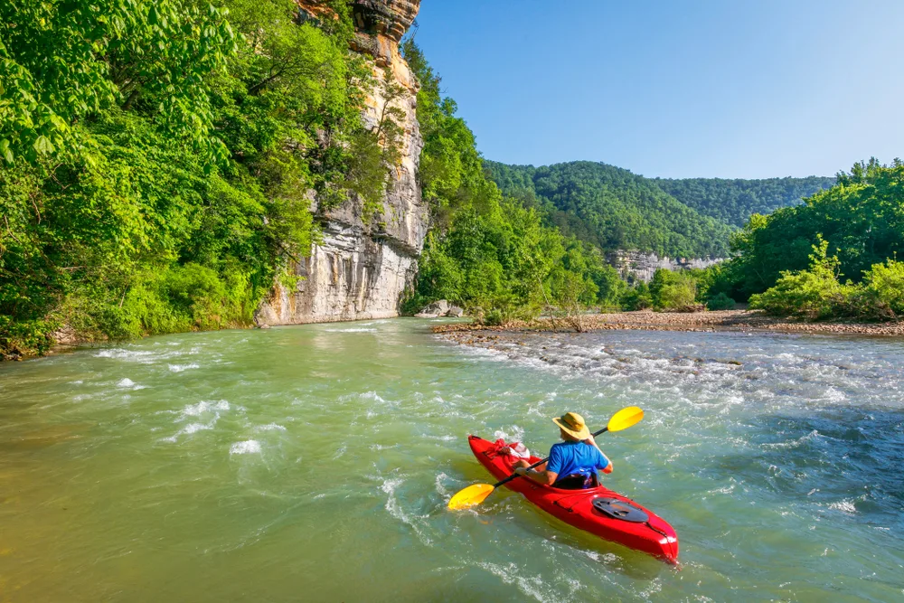 Kayaker floats down the river near Ponca in his red kayak with a blue hat for a guide to the best time to visit Arkansas