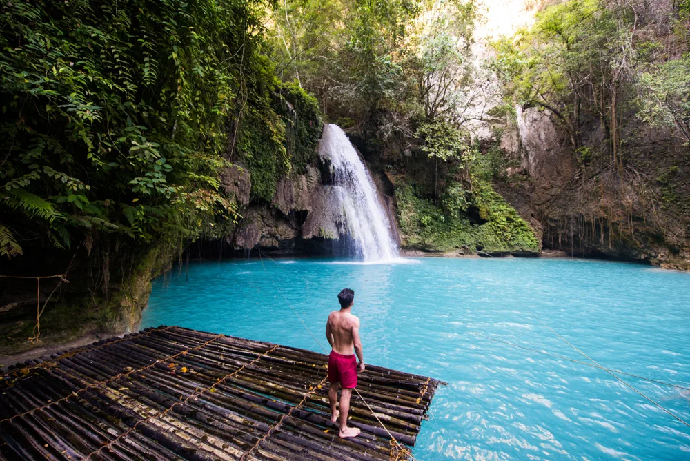 Man on a raft pictured floating towards a waterfall that is making its way into a very blue lagoon during the best time to go to the Philippines