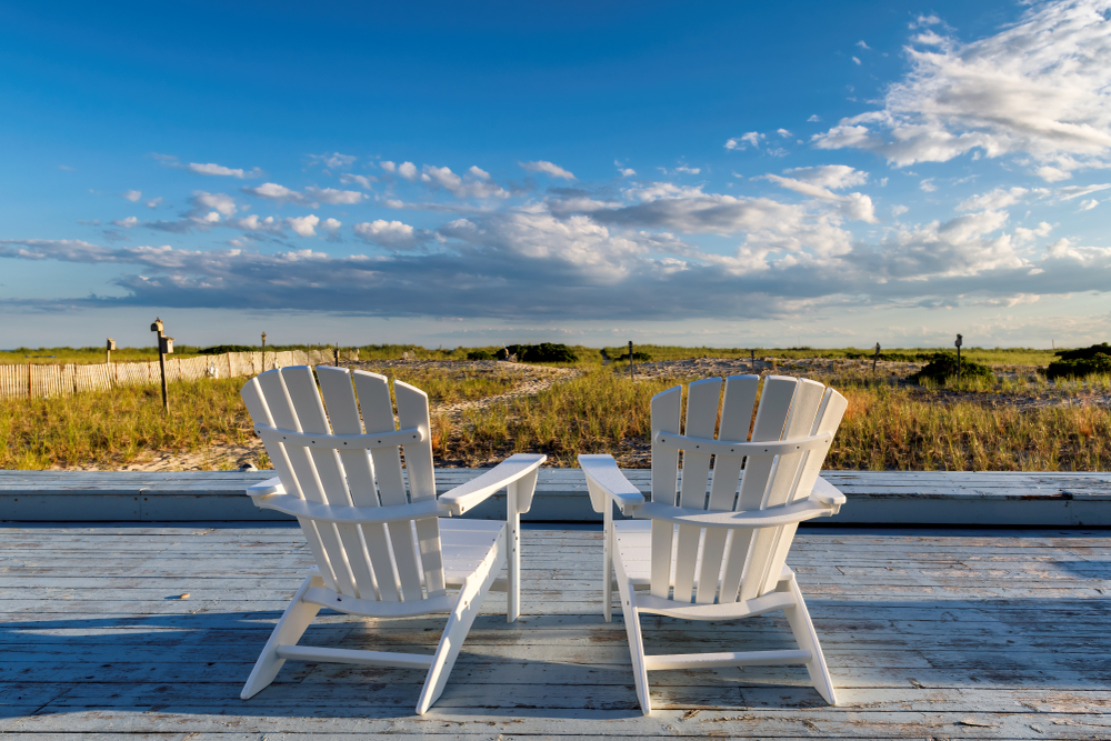 Two white beach chairs on a wooden deck overlooking a marsh with a few clouds in the sky for a piece on the best time of year to visit Cape Cod