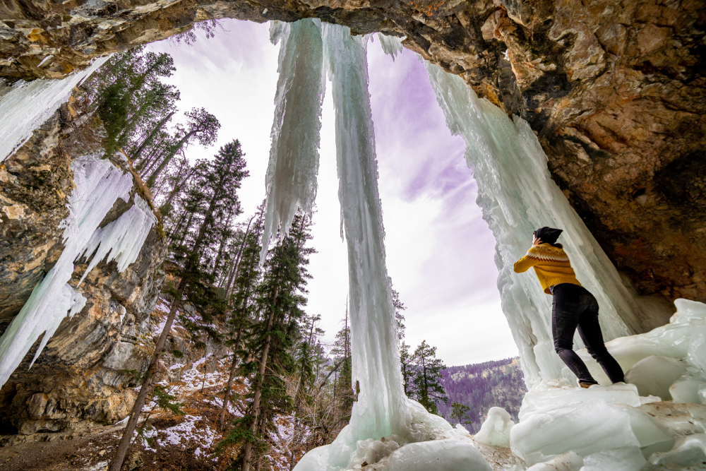 Woman in a yellow shirt pictured standing below a frozen waterfall during the cheapest time to go to South Dakota