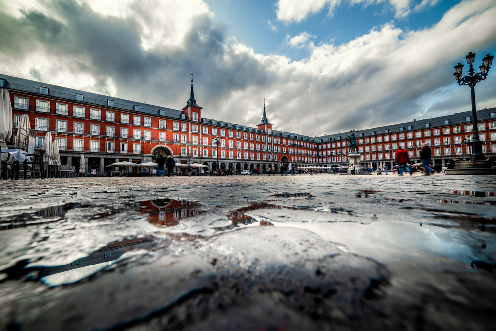 Rain clouds over a red brick palace, as seen from the ground during the rainy season, the cheapest time to visit Madrid