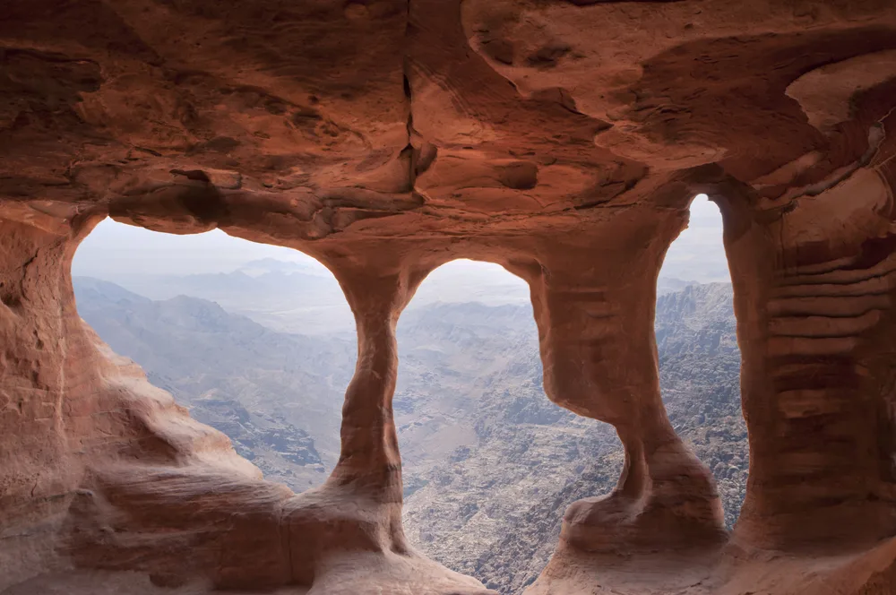 Rock openings carved in with a distant view of Petra Jordan