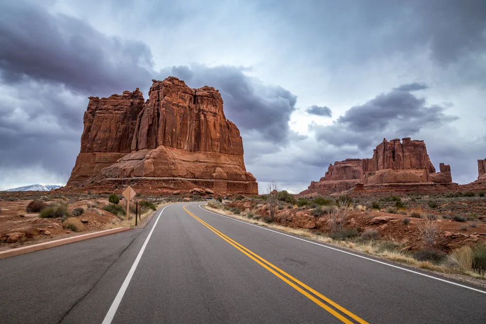 Rain cloud looming over the butte, as seen from the view of a driver on a road during the cheapest time to visit Arches National Park