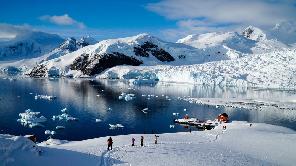 Paradise Bay pictured with lots of visitors on the ice looking at the wildlife during the best time to visit Antarctica with blue skies and deep blue water