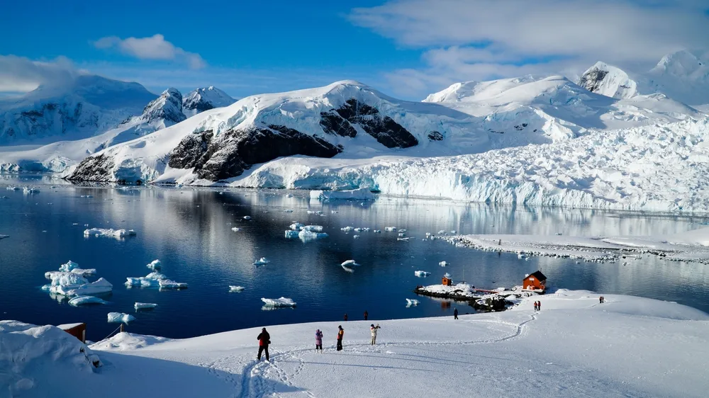 Paradise Bay pictured with lots of visitors on the ice looking at the wildlife during the best time to visit Antarctica with blue skies and deep blue water