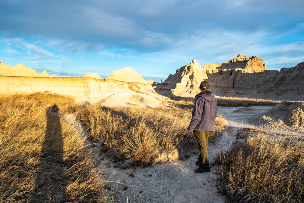 Man standing in South Dakota's Badlands National Park wearing a coat and long khaki pants during the best time to visit the park